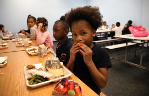 Kids eat a meal of chicken, green beans, fruit and more.