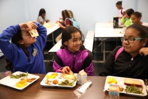 Girls goof around as they eat their meal.