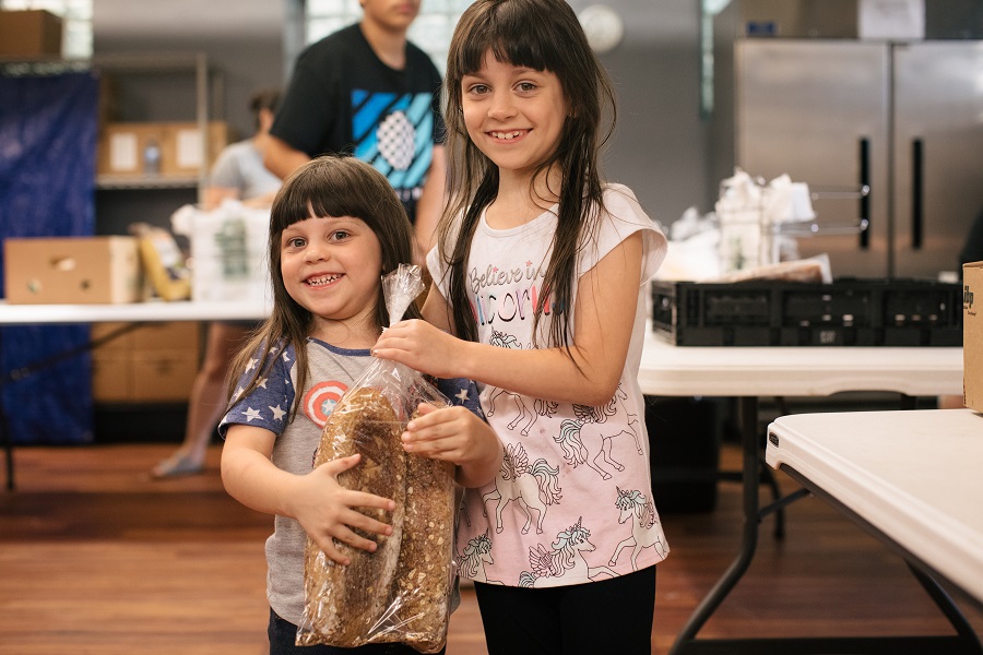 Two girls pose with loaves of bread at the food pantry.