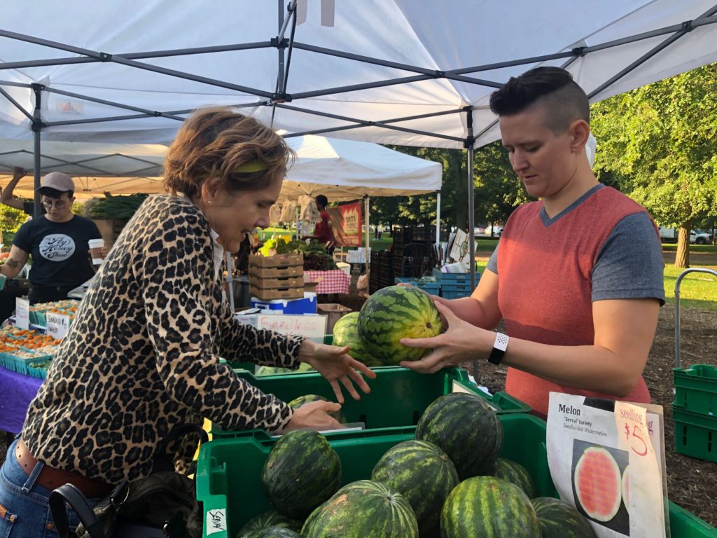 Student Sonia Mantell purchases a melon at the stand from Seedling Farm of South Haven, Michigan