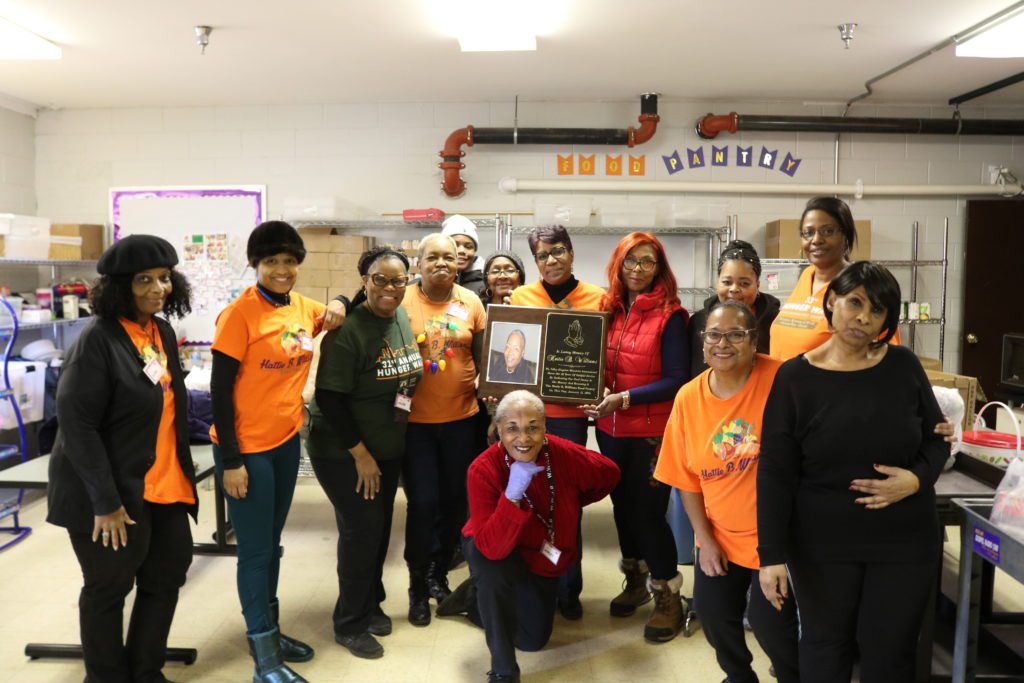 The volunteers of the Hattie B. Williams food pantry pose with a plaque made in Williams' honor.