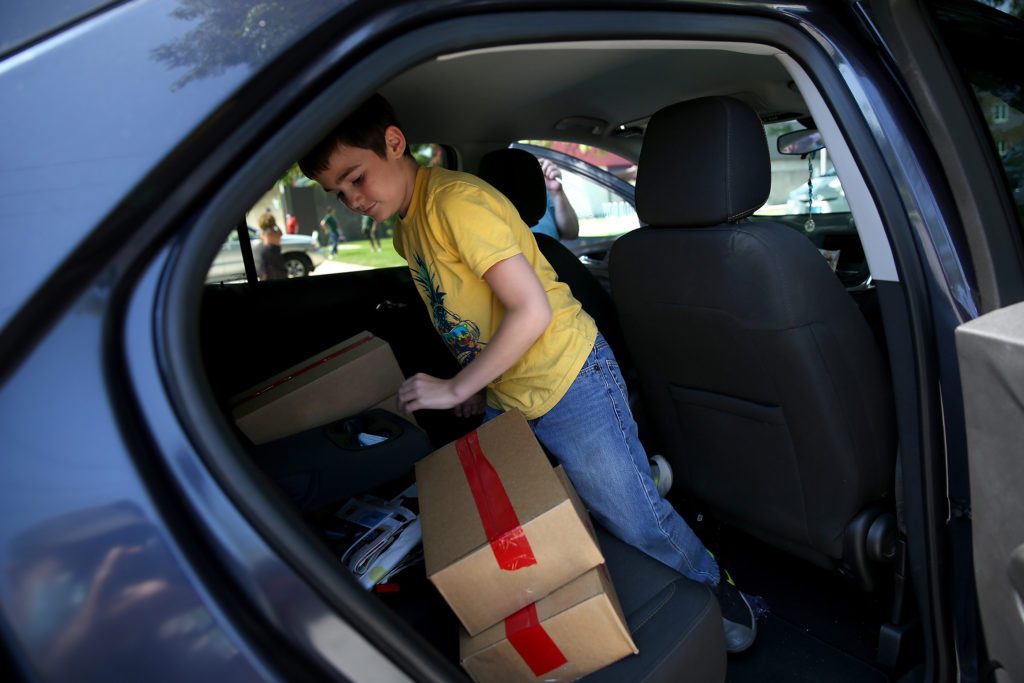 A young boy puts boxes of meals in his mother's car for him and his sister at the Lansing Lunch Bus site
