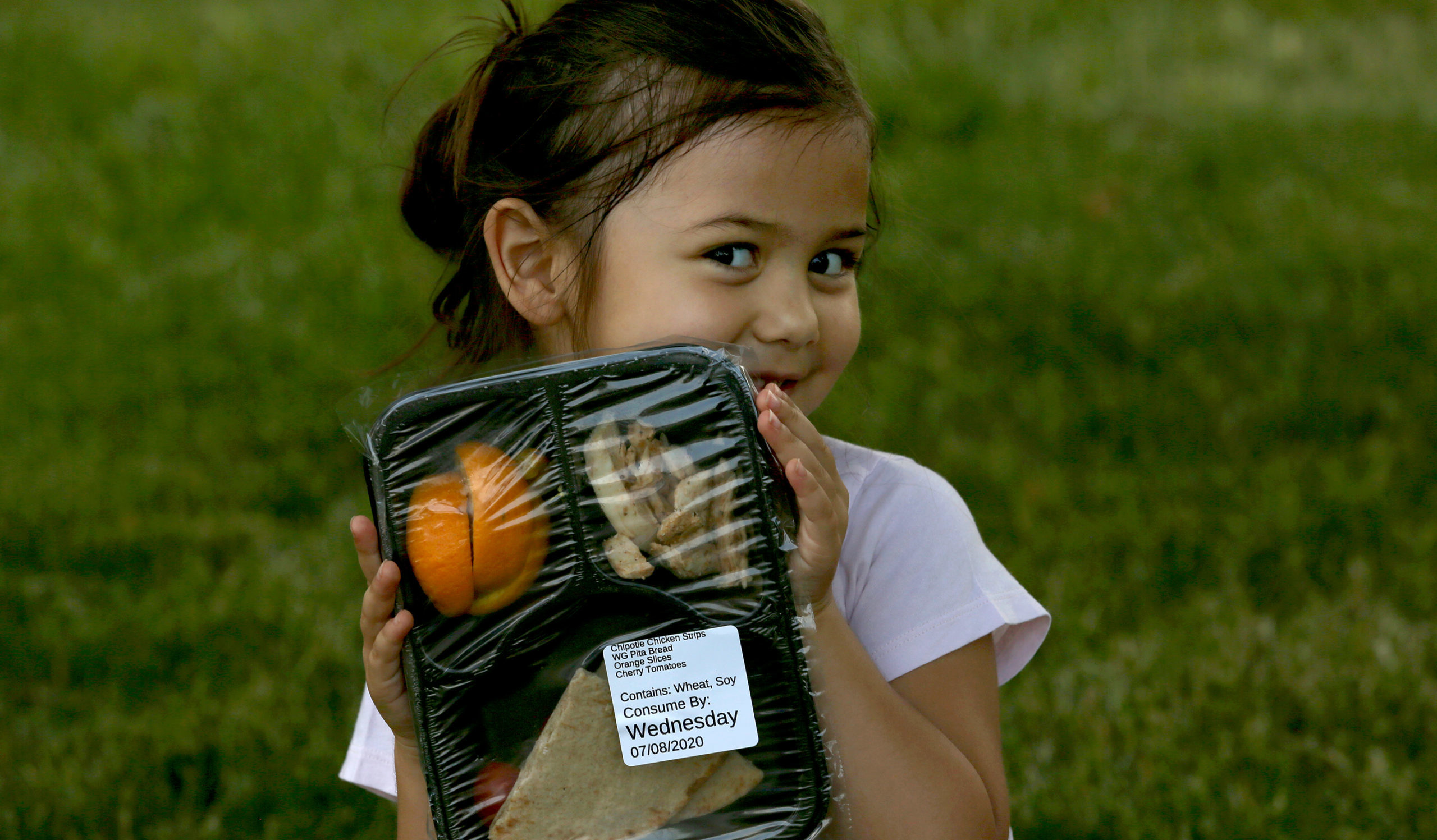 A young girl eats lunch with her mother and two sisters at the park next to the Berwyn Township public health building, where the Food Depository's Lunch Bus parks three days a week.