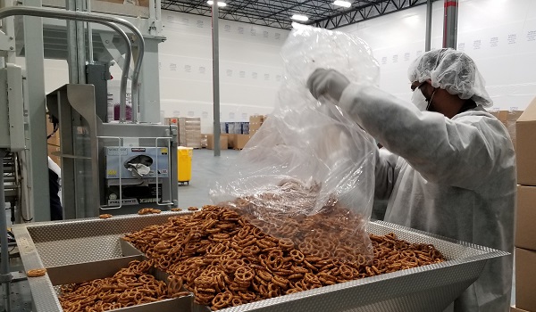 A CREDMADE worker loads a large batch of pretzels into the packing machine.