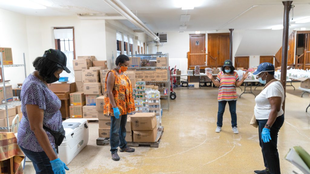 Joyce Gittens (center) leads a prayer with the volunteers before a recent distribution. The church's Fellowship Hall has been used to store extra food since the start of the pandemic.