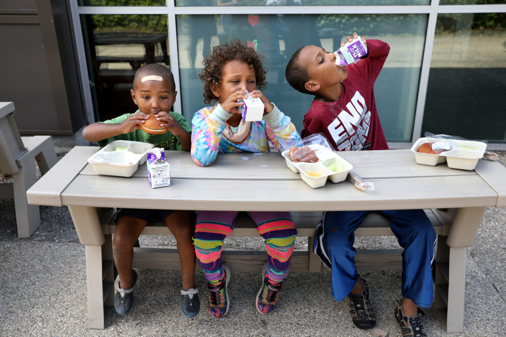 Zakariah, Gabby and Ebbah eat their meals at the Lansing Lunch Bus stop