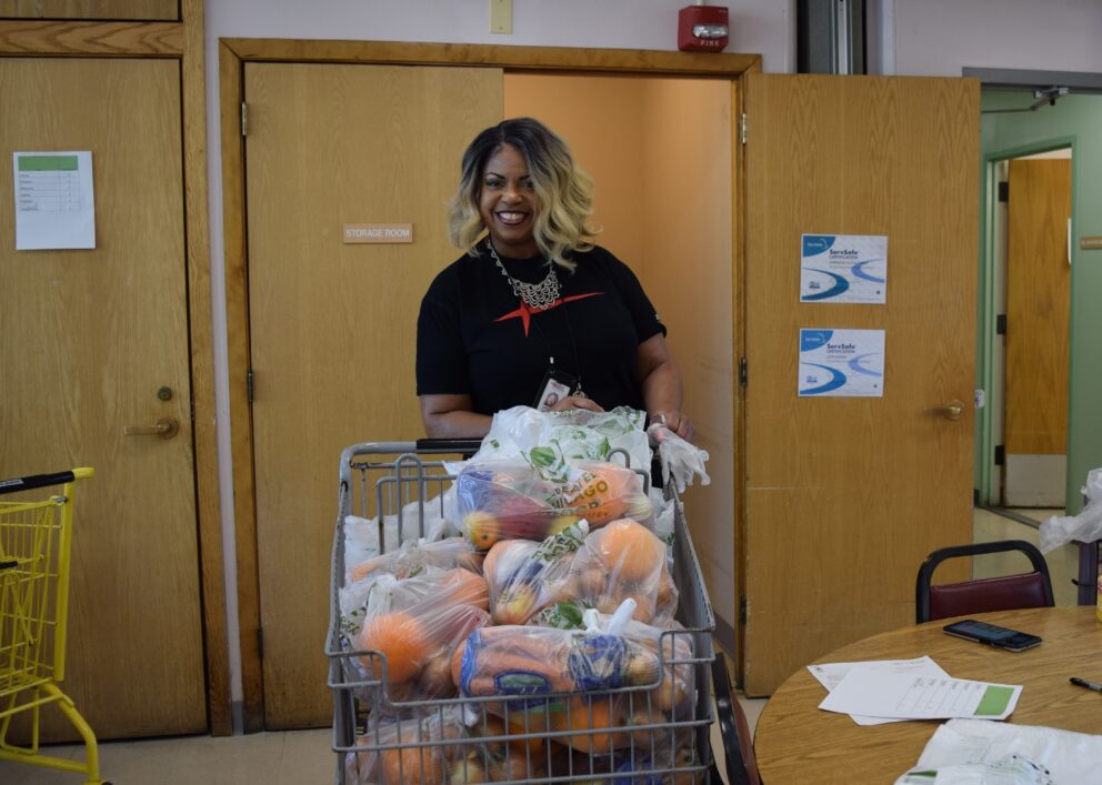 a smiling woman stands behind a full grocery cart