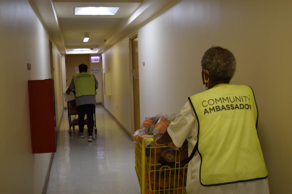 two women push full grocery carts down an apartment hallway