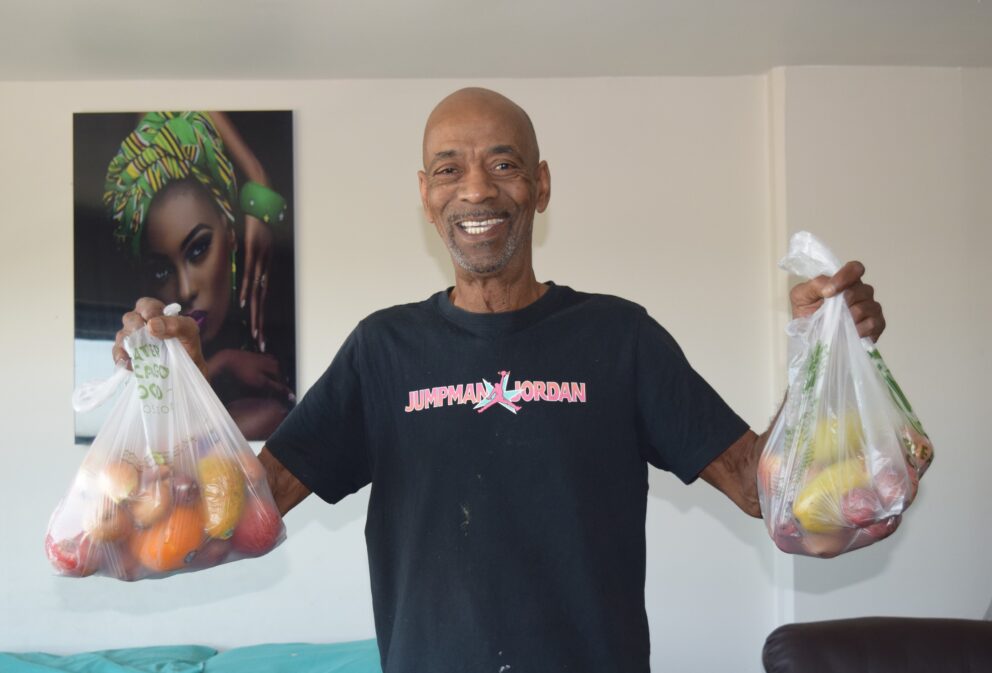 a smiling man holds up two bags of groceries