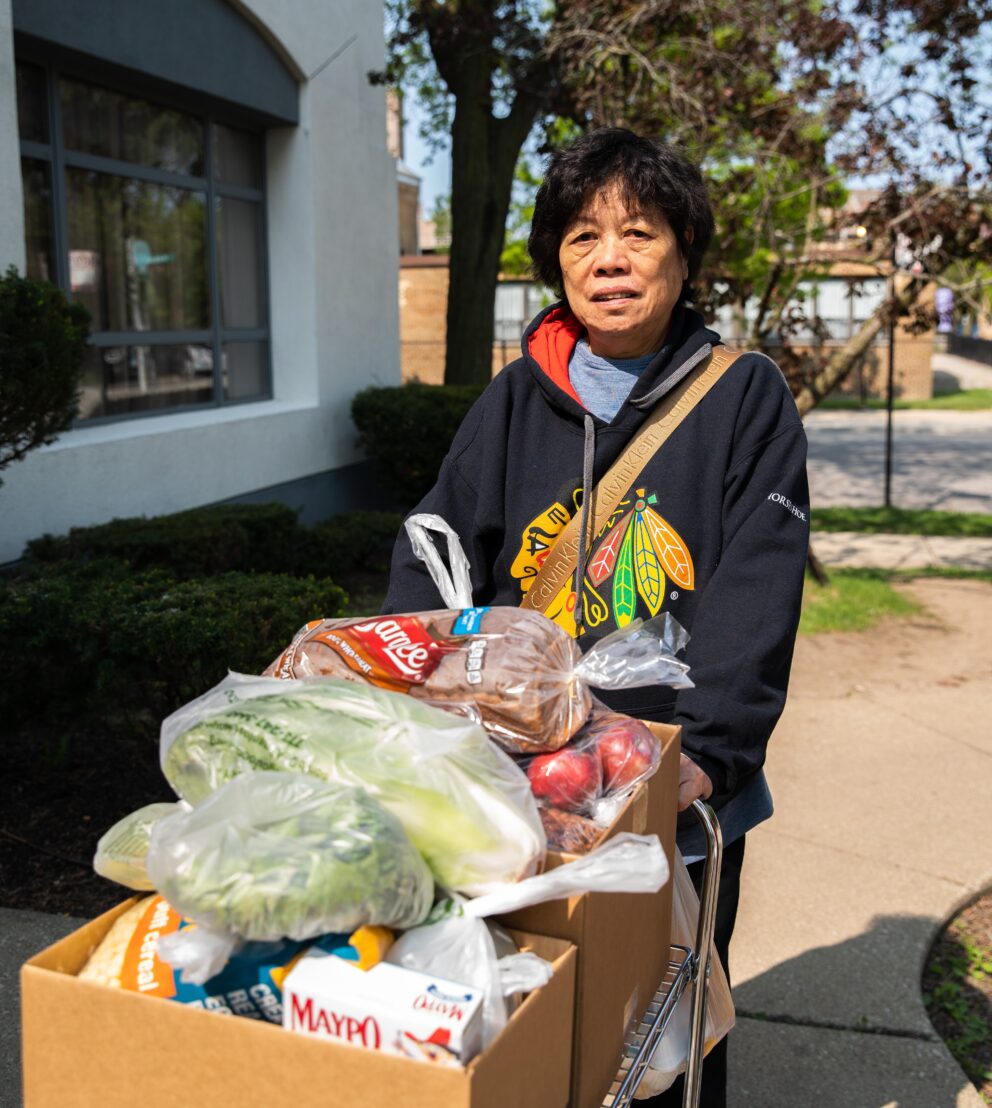 a woman stands outside with a box full of groceries