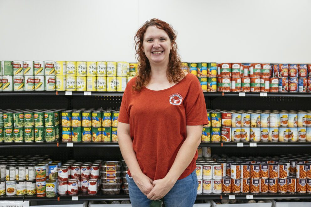 a woman stands in a food pantry smiling at the camera