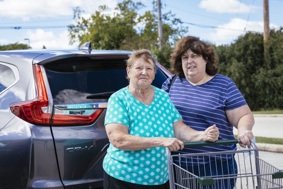 two women stand at their car with a grocery cart