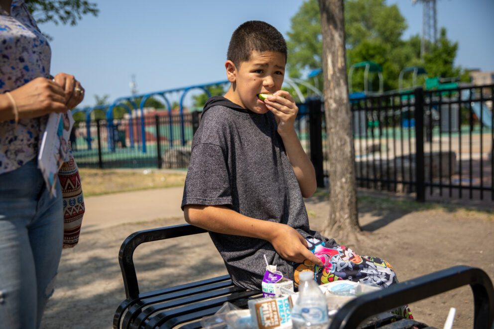 a boy eats lunch on a bench