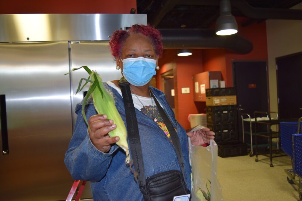 a woman at a food pantry holds up an ear of corn