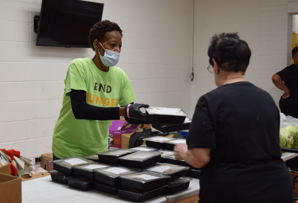 a woman hands a couple of prepared meals to a pantry guest