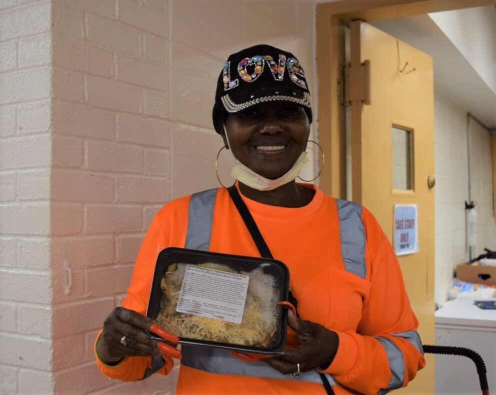 a woman holds up a prepared meal and smiles