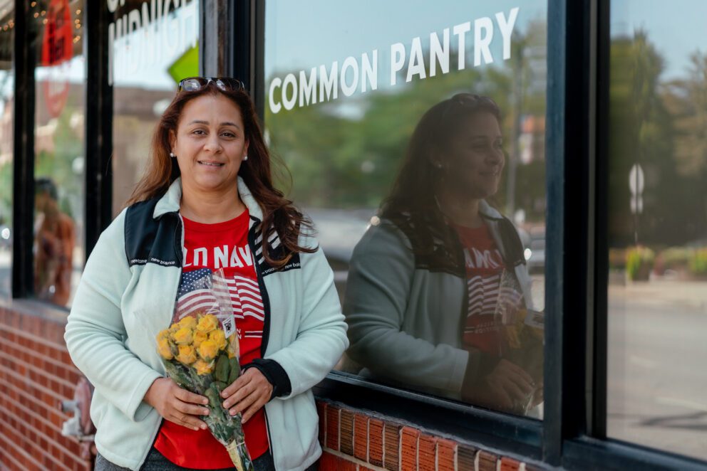 a woman stands in front of a food pantry holding flowers
