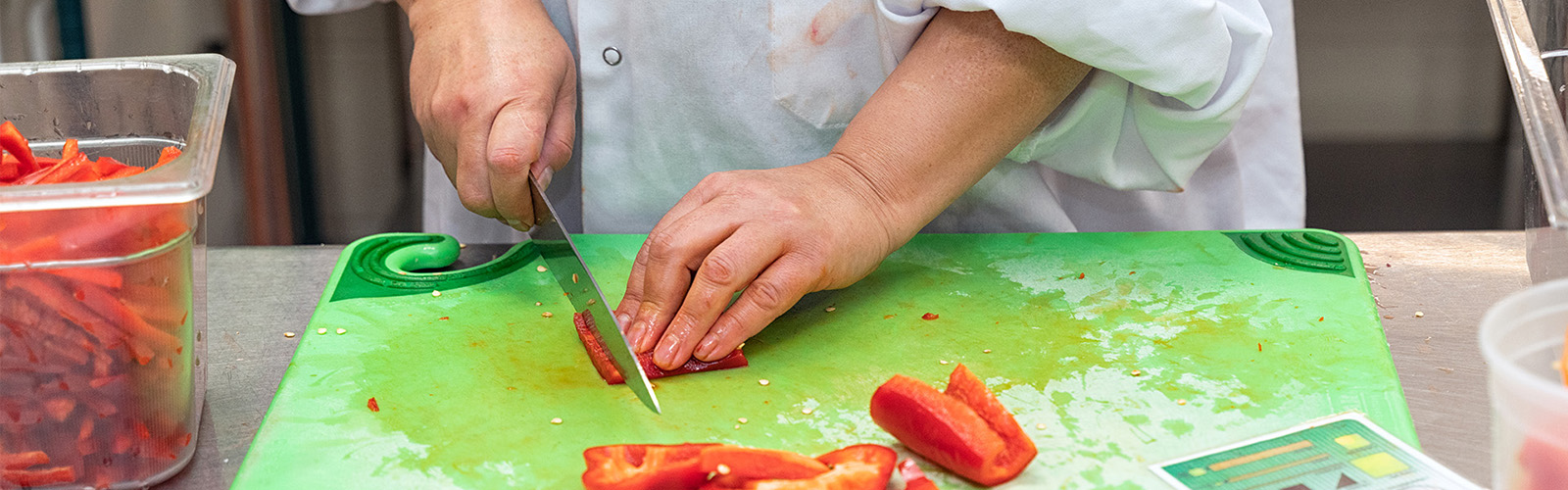 Chef with knife slicing red peppers.