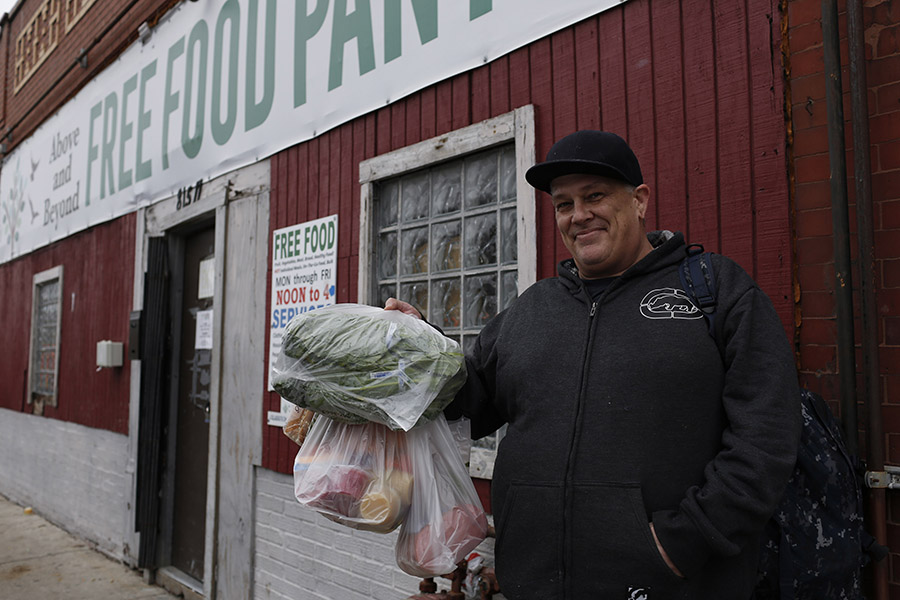 A man holds up bags of food in front of a food pantry.