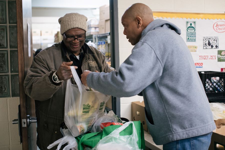 Pantry guest receiving bags of fresh fruit and canned goods.