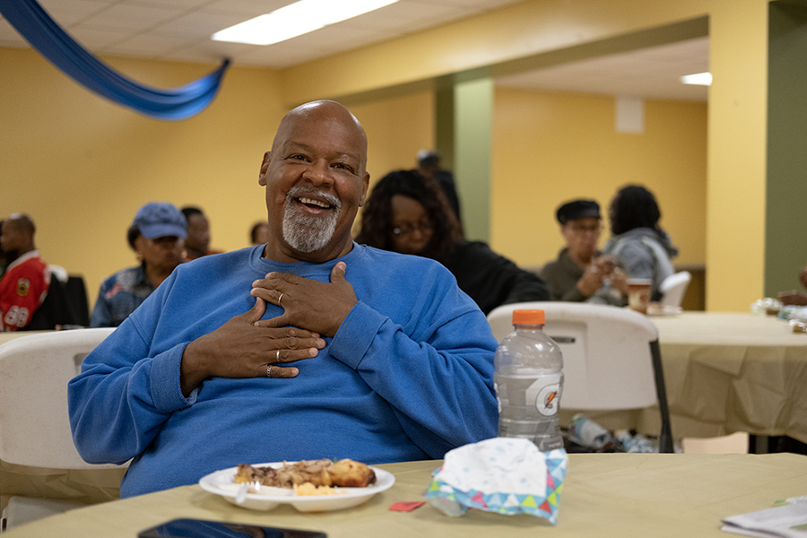 a man is smiling as he sits down to a meal at a soup kitchen