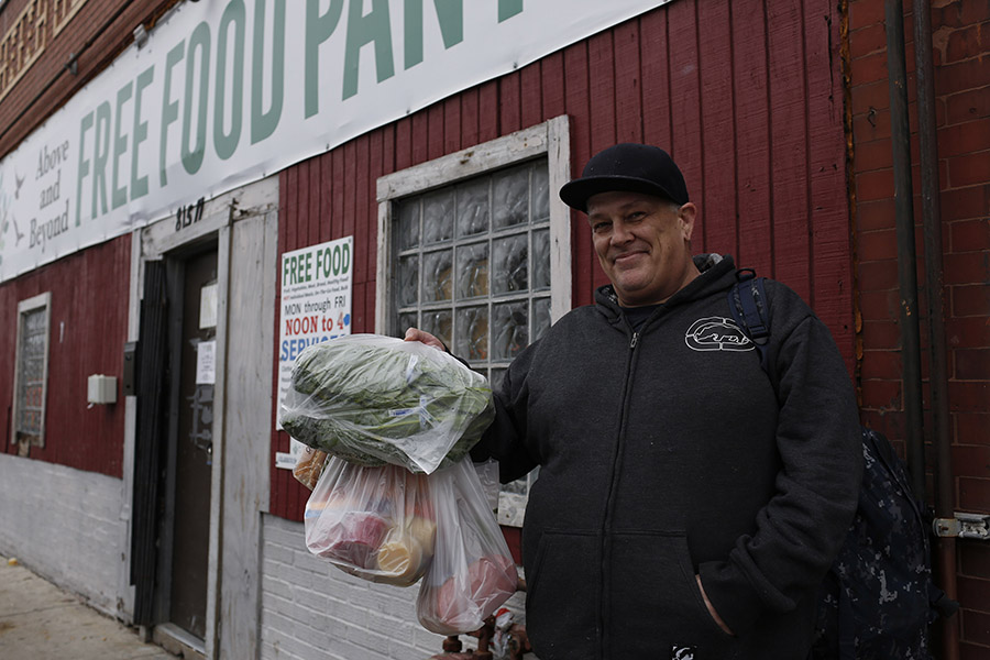 a man holds up a bag of groceries outside a food pantry
