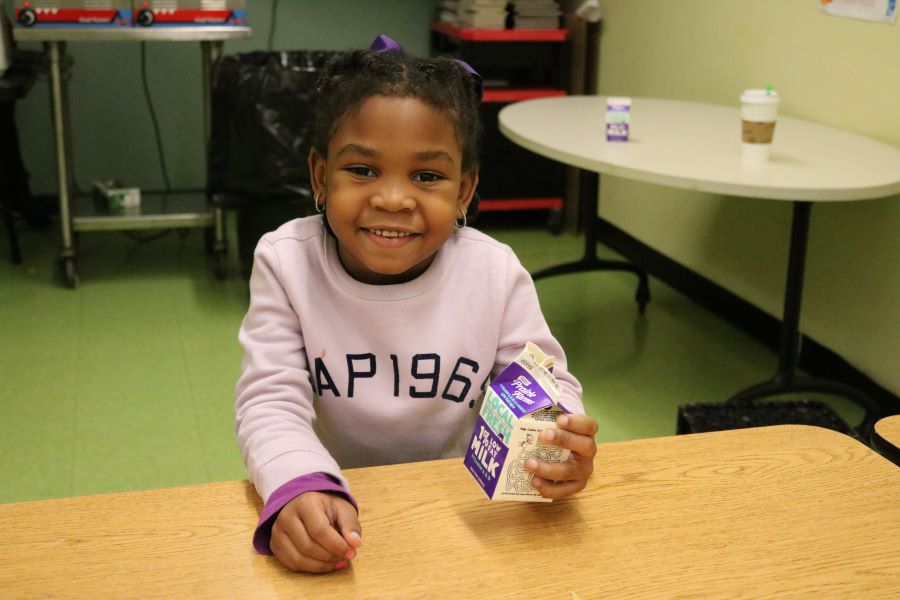 A girl sits a table drinking milk.