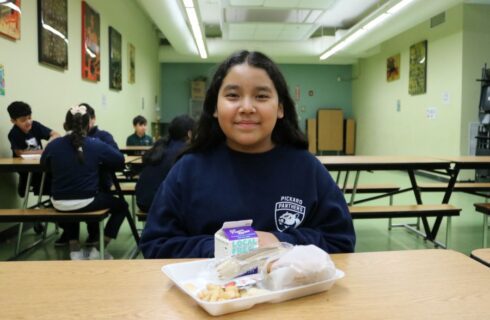 A girl sits at a table with food in front of her.