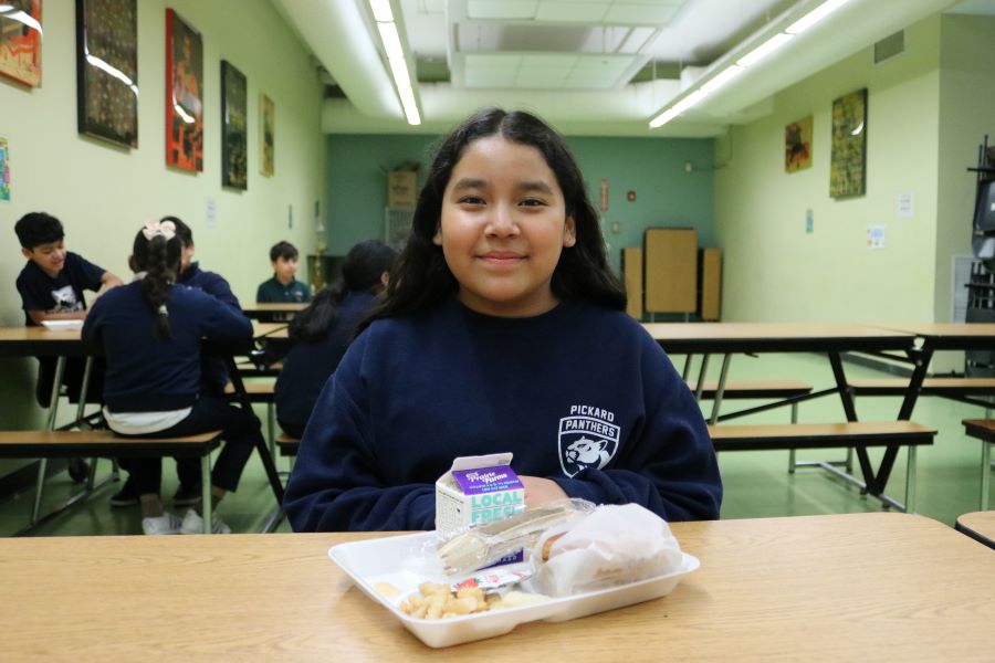 A girl sits at a table with food in front of her.