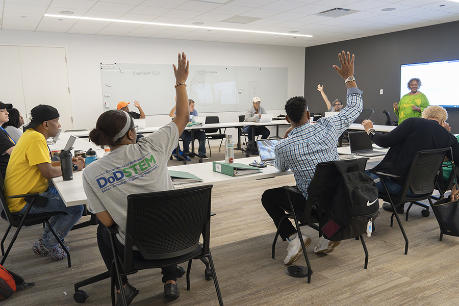 adult students in a classroom, a few raising their hands