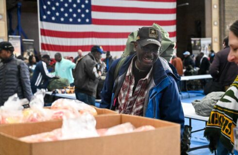 A man smiles in front of an American flag