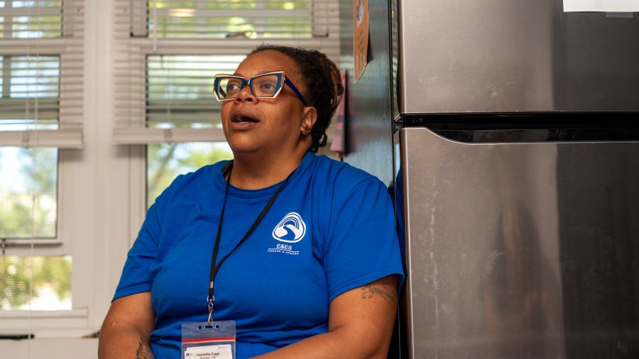 A woman in a blue t-shirt sits and talks.