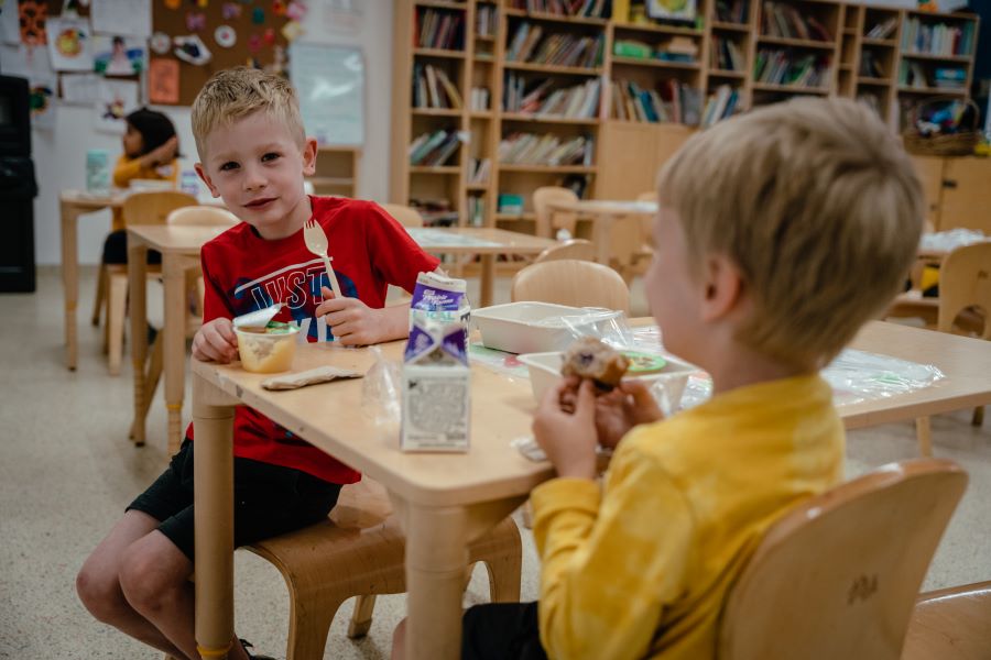 Two boys sit at a table and eat a meal.