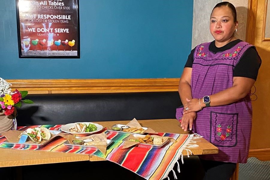 A woman stands next to a table of food.