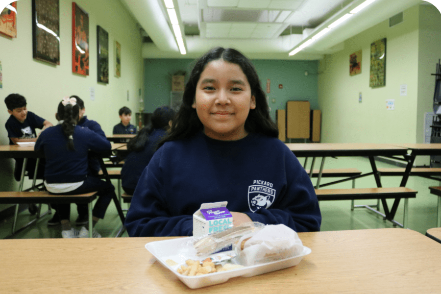 Young girl sits at a lunchroom table enjoying a meal.