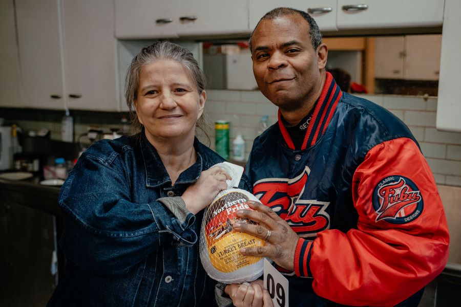 A couple holds a turkey and smiles at the camera