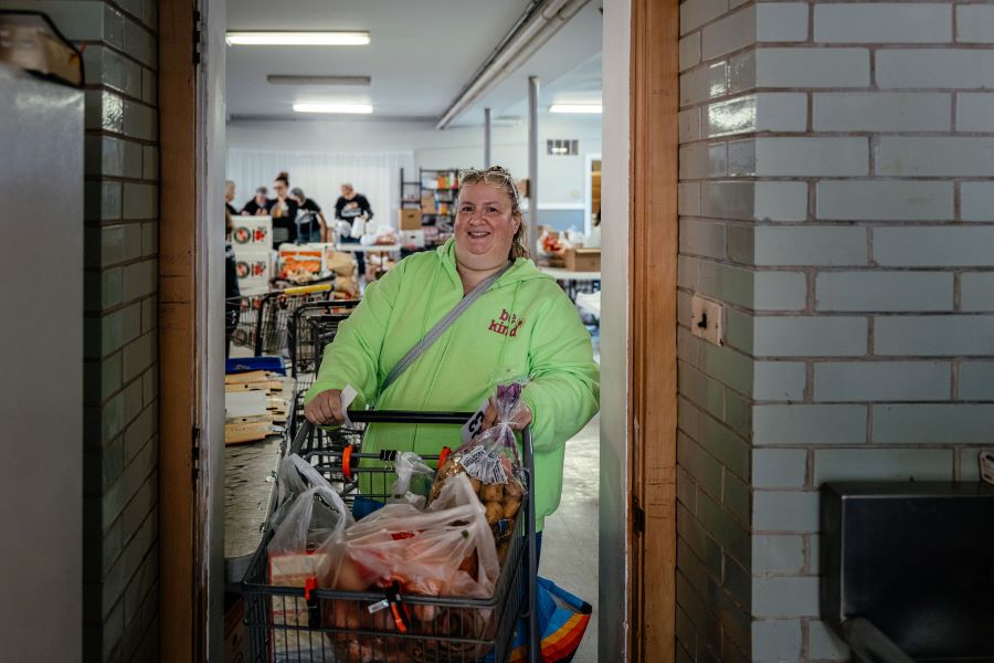 A woman smiles at the camera as she stands with a full shopping cart. 