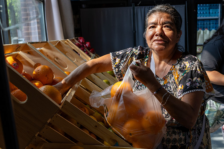 A woman smiles at the camera as she selects oranges from a food pantry