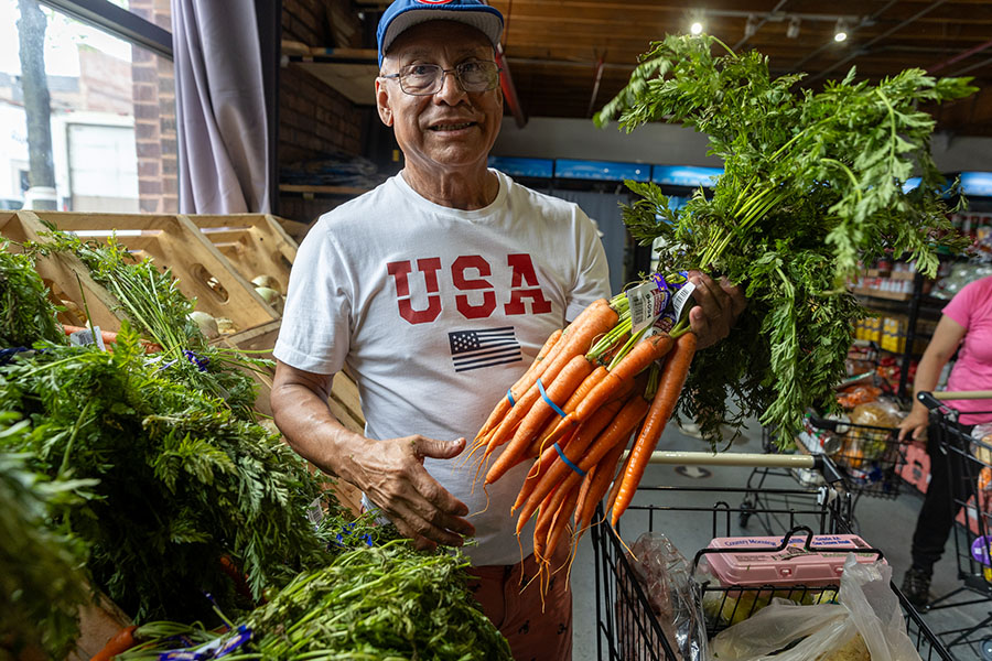 An older man holds a bunch of carrots and smiles at the camera
