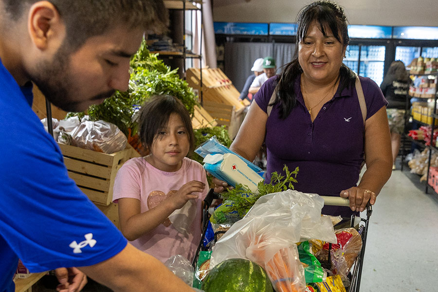 A mother and daughter watch as a volunteer places food in their cart