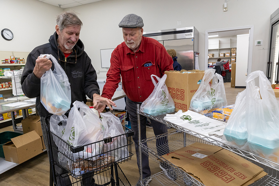 A man helps load groceries into another man's shopping cart.