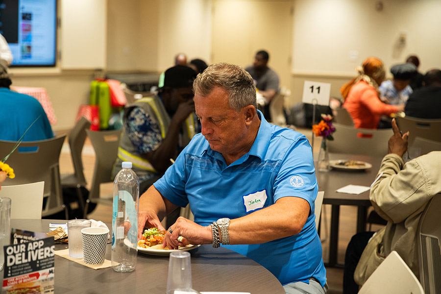 a man in a blue shirt eats dinner in a room full of guests