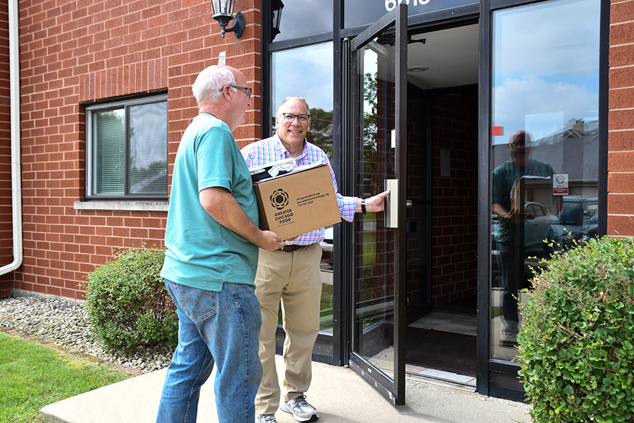 a man holds open a door for another man holding a box of prepared meals