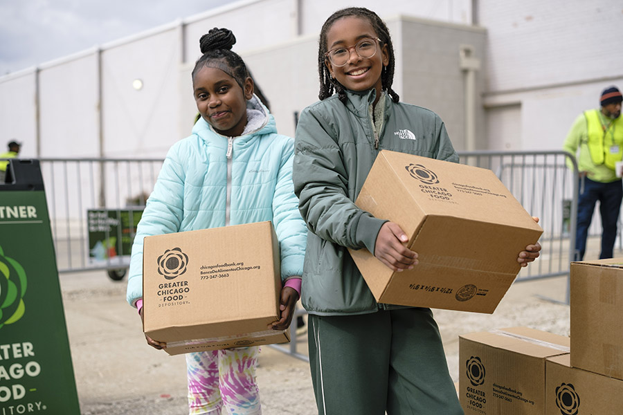 Two young volunteers stand smiling and holding food boxes