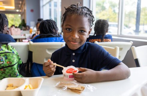 A young boy is eating yogurt and smiling at the camera