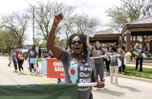 a woman with her fist raised marches in a Save Our SNAP rally
